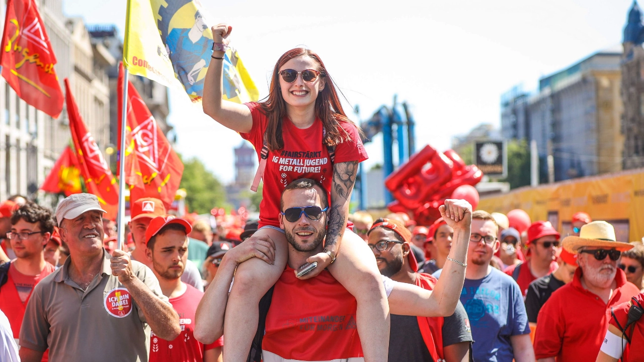 Junge Frau sitzt auf den Schultern von einem jungen Mann. Beide heben kämpferisch die Faust nach oben.