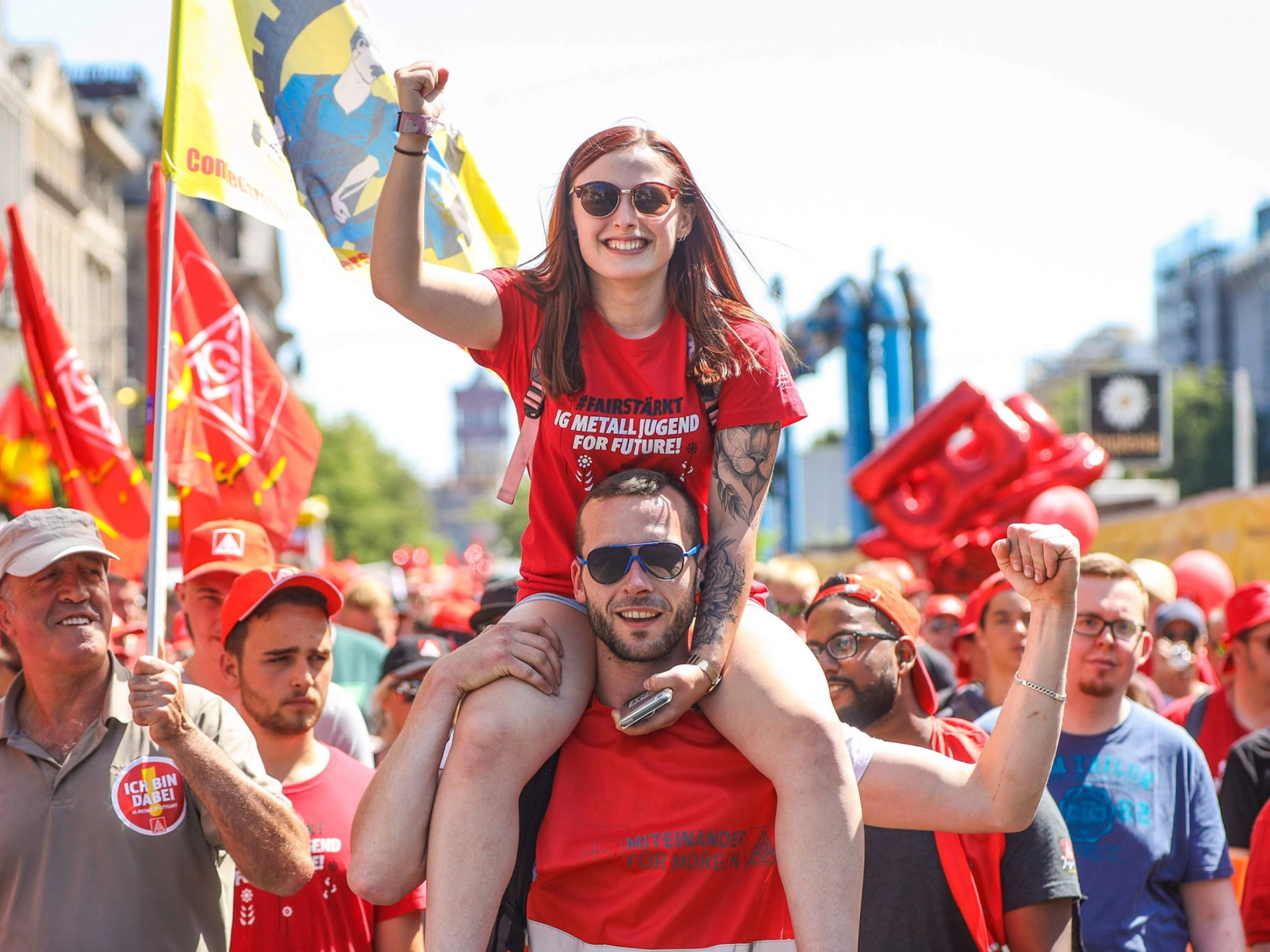 Junge Frau sitzt auf den Schultern von einem jungen Mann. Beide heben kämpferisch die Faust nach oben.