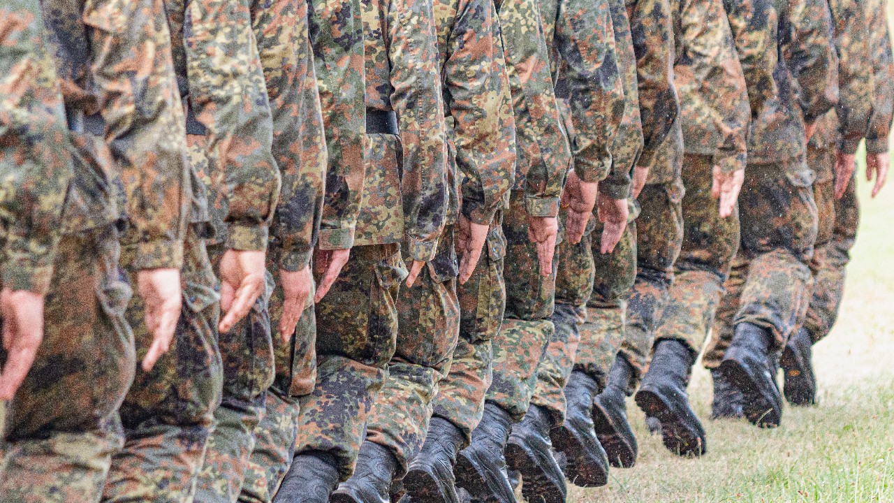 Soldaten der Bundeswehr marschieren im Gleichschritt über eine Wiese.